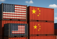 U.S. & China Tariff War: What to Know Stacked shipping containers painted with U.S. and Chinese flags, set against a blue sky with clouds, symbolizing trade conflict between the two nations.