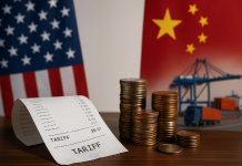 What U.S. Tariffs Really Cost You A crumpled receipt labeled “TARIFF” lies on a table in the foreground, with a U.S. flag and Chinese flag behind it. Stacks of coins and shipping containers blur in the background, representing trade, economic tension, and policy impact.